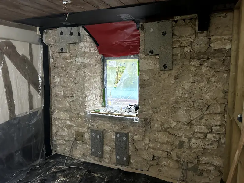 Bare stone wall before insulation, with a small window and steel plates fixed to the stonework