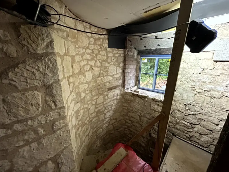 Corner of bare stone walls with a window, protective sheeting on the floor