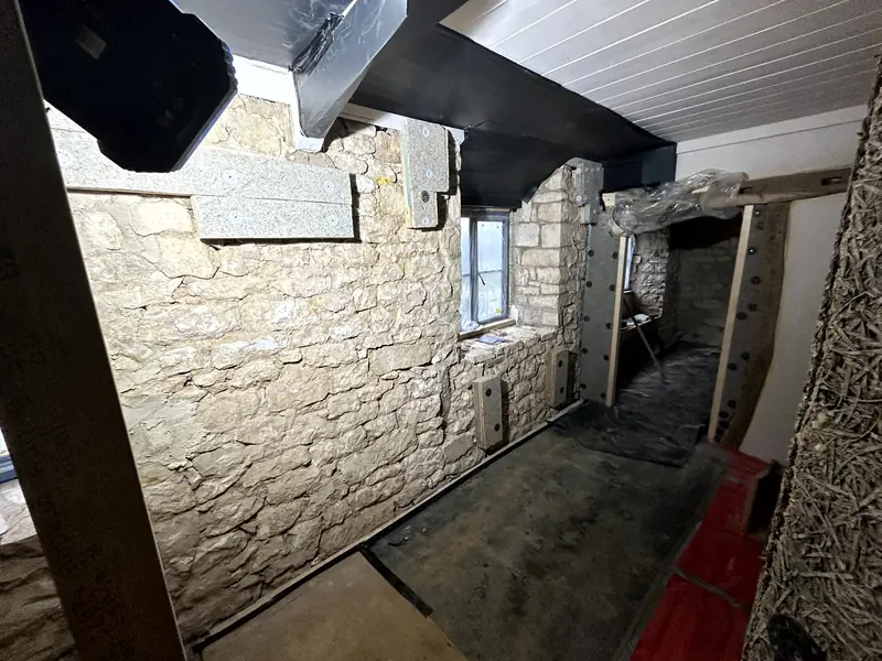 Narrow room with bare stone walls and a timber prop, before insulation