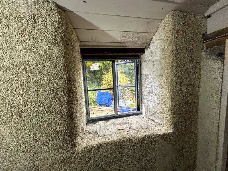 Deep window reveal wrapped in sprayed hempcrete, the wall following the stone beneath