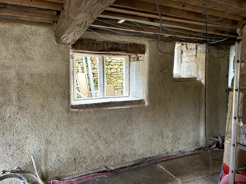 Room with sprayed hempcrete on the walls under exposed oak beams, two windows set deep in the wall