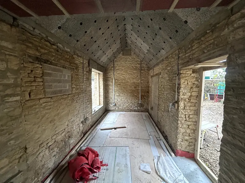 Long Cotswold stone outbuilding before insulation, vaulted roof above and boards on the floor