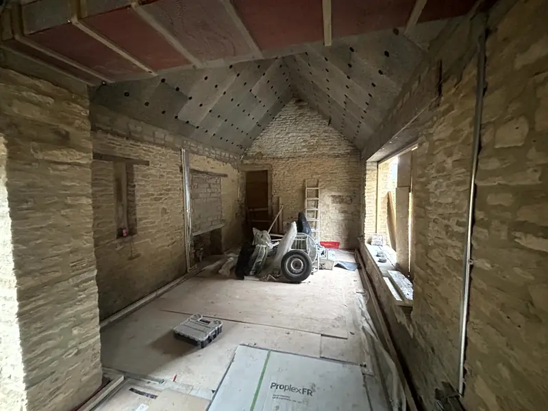 Bare stone walls and window openings in the outbuilding before hempcrete, materials stacked inside