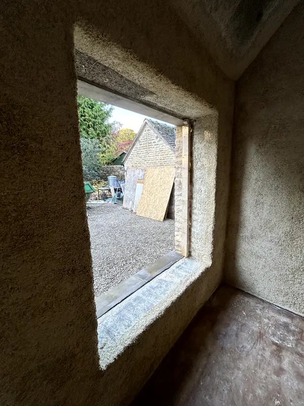Deep window reveal finished in sprayed hempcrete, looking out to the stone house next door