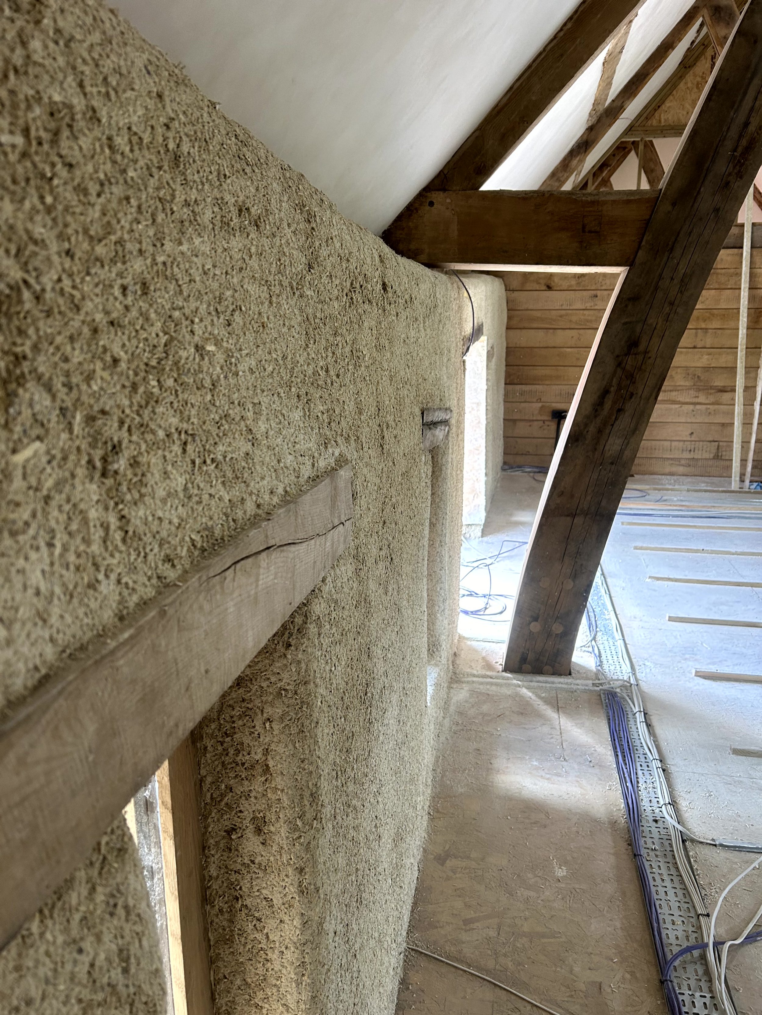 Sprayed hempcrete following the curved edge of a barn wall up to an exposed oak beam