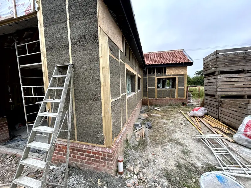 External wall of the barn showing cast hempcrete between the timber studs, ladder and site materials alongside